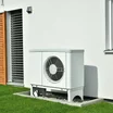 white heat pump unit outside home with green lawn and white walls