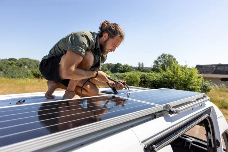man on the roof of a camper van, connecting black solar panels