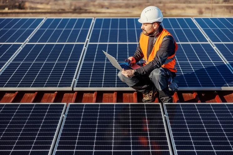 Someone in an orange high vis jacket testing blue solar panels in a solar farm