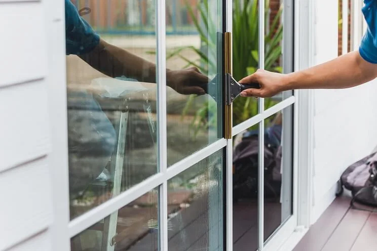 Window installer on porch cleaning a large window with white frames