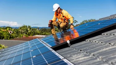 Solar panel technician in orange with drill installing solar panels on a roof