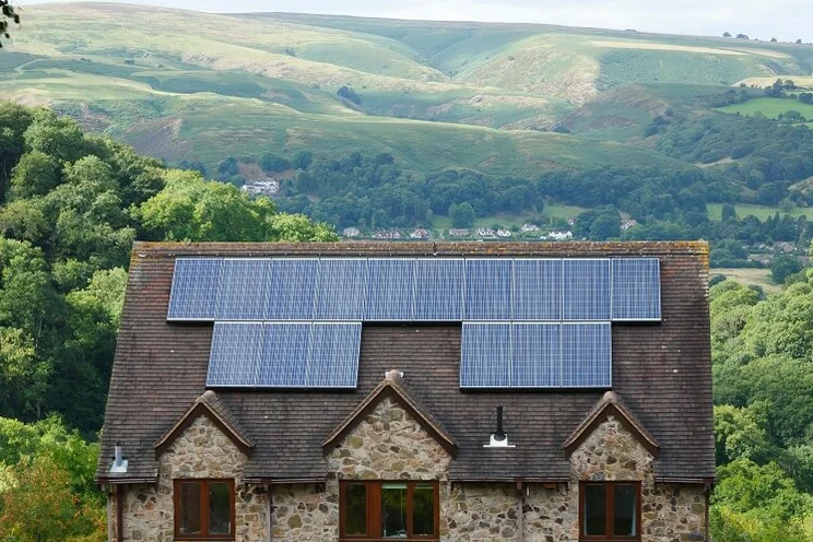 Blue solar panels on a grey stone house in the countryside with fields in the background