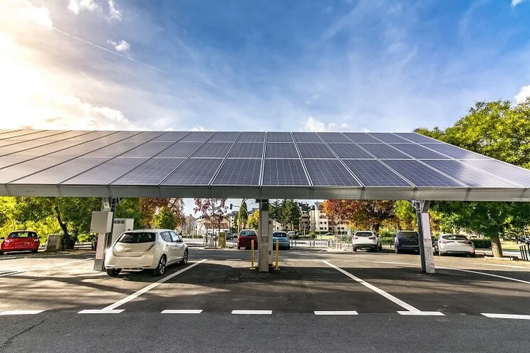A white car parked in a car park covered by lots of blue solar panels overhead