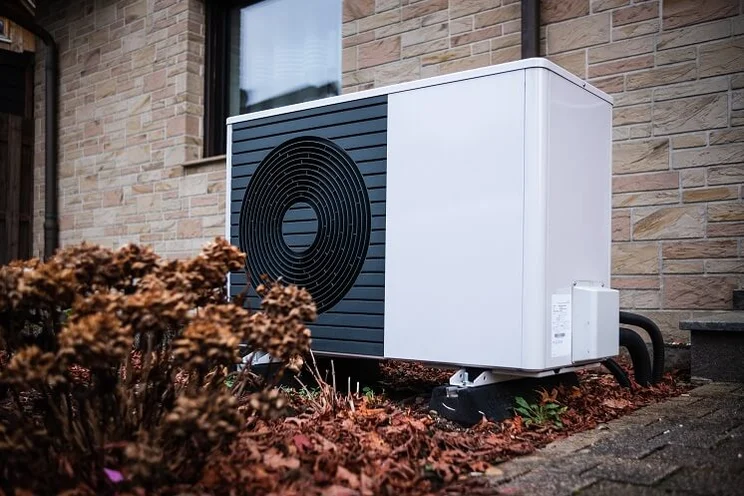 Air source heat pump unit outside a home surrounded by autumn leaves