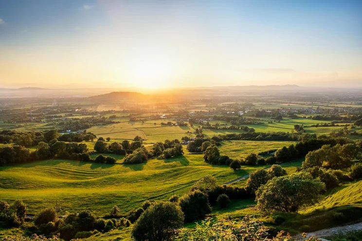 sunset over green fields and trees seen from a hill