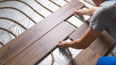 man placing wood boards over underfloor heating pipes