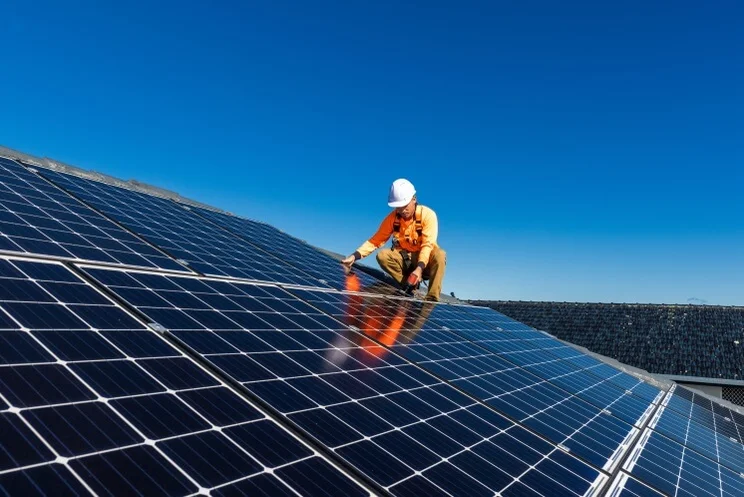 Solar panel technician with drill installing solar panels on a roof