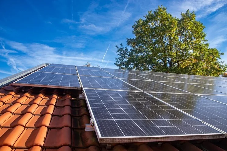 solar panels on red tile roof with blue sky and tree in background