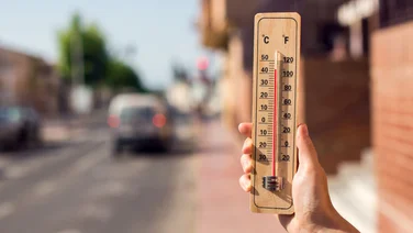 Thermometer in hand in front of an urban scene during heatwave.