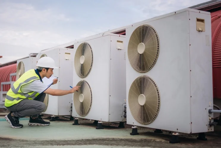 an engineer in a fluorescent jacket checking on heat pumps on a roof