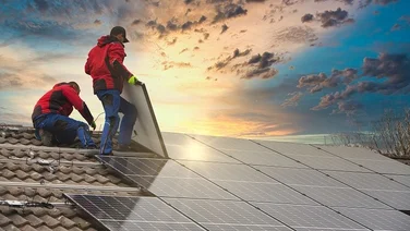 Two people installing solar panels on a roof with a sunset in the background