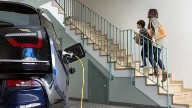 Electric car charging in a family home as a parent and her child walk upstairs