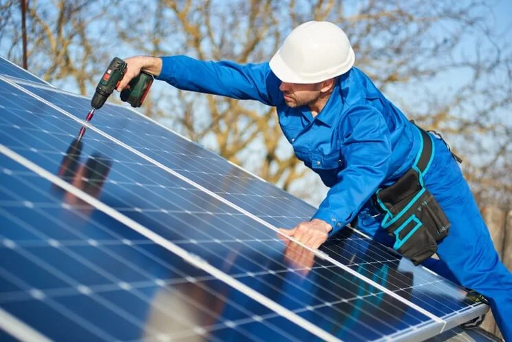 an installer in a blue jumpsuit secures a solar panel with a tool