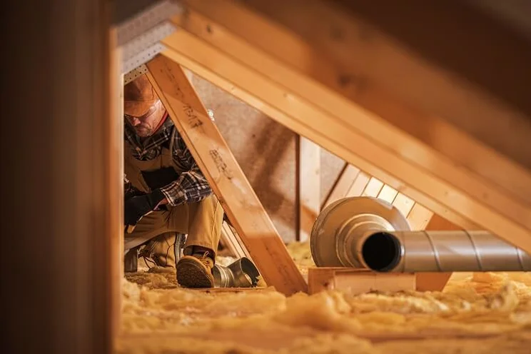 Installer in yellow overalls pays out roll of insulation in roof