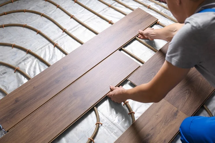 man placing wood boards over underfloor heating pipes