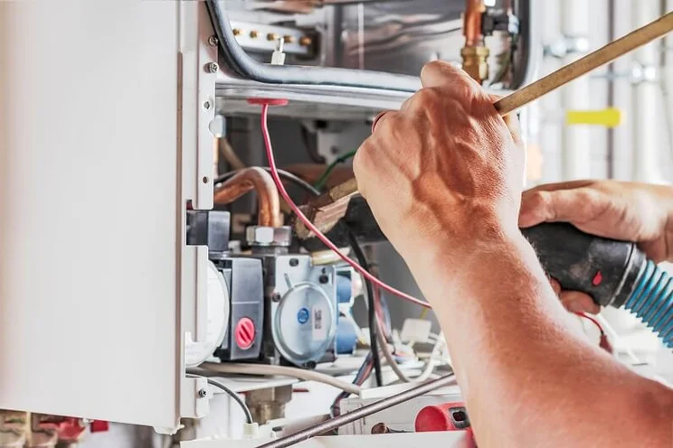 Close up image of a person servicing a boiler, with the internal components clearly visible