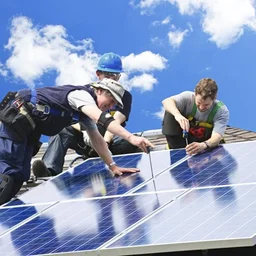 three people installing solar panels on a roof, against a blue sky