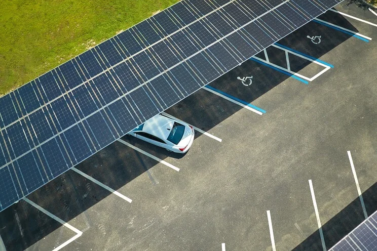 A birds eye view of a white car parked under a stretch of blue solar panels
