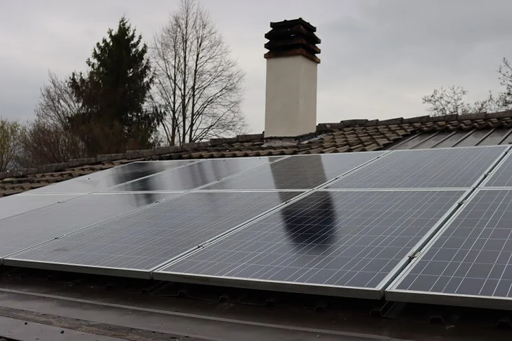 Solar panels on the rooftop of a house in winter, with grey sky and bare trees in background