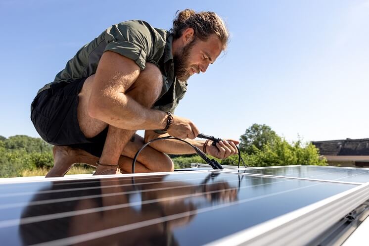 Homeowner installing a DIY solar panel on roof on a sunny day