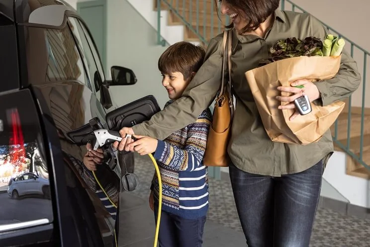 mother and son charging electric car in garage