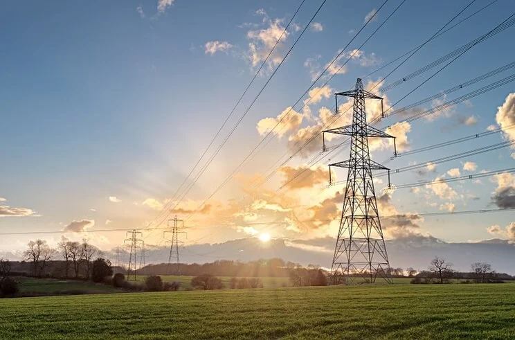 A silhouette of an electricity pylon against a blue sky in the English countryside