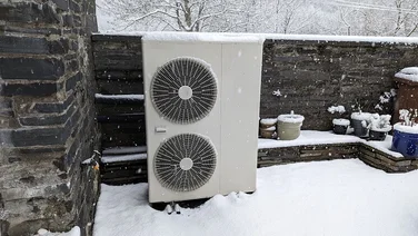 outdoor unit of heat pump against stone wall in snowy garden