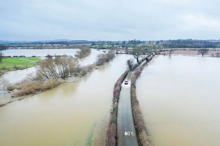 car driving on road with flooded fields on either side
