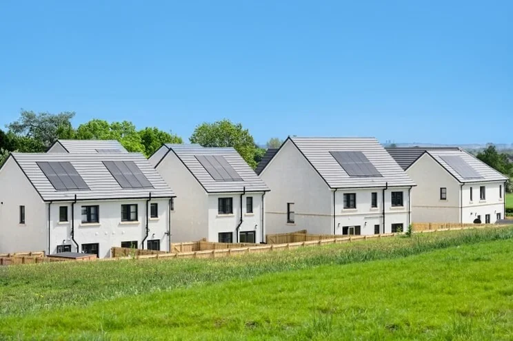 homes with solar panels in front of green grass, under a blue sky
