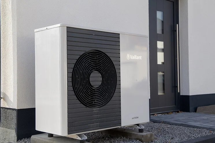 air source heat pump outside house with gravel entrance and white walls