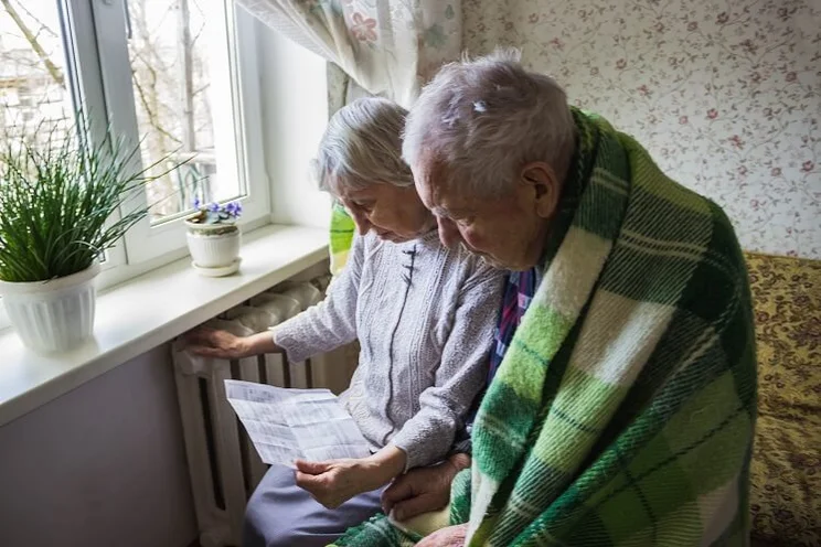 elderly couple huddled by radiator looking at energy bill