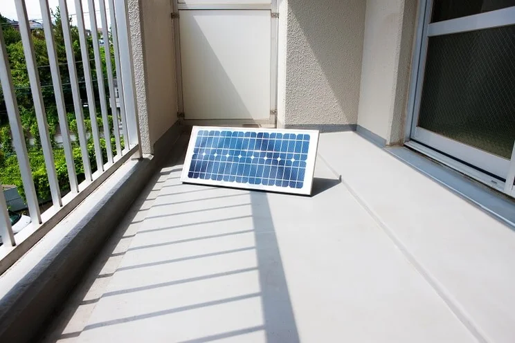 small portable solar panel in sun on balcony with white metal railing