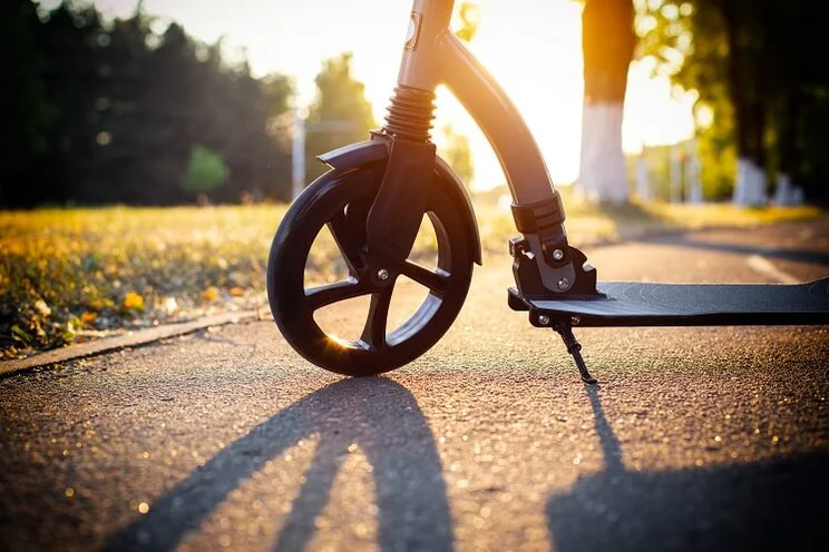 close up of front wheel of an electric scooter on road with sun setting in background