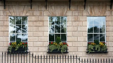 row of three white, rectangular sash windows with flower pots in front in brown stone building