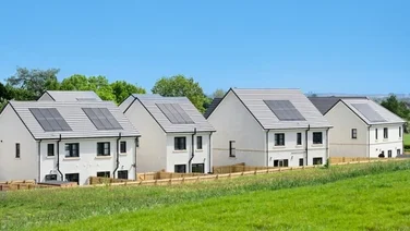 homes with solar panels in front of green grass, under a blue sky