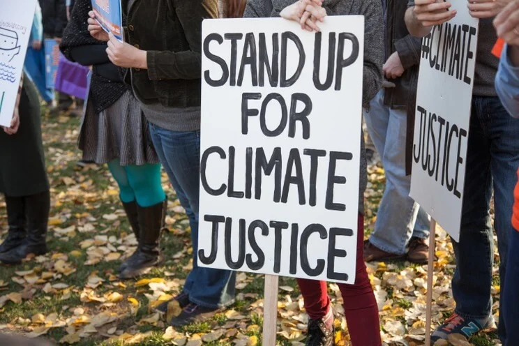 a protest sign with the text 'stand up for climate justice' in front of some people's legs