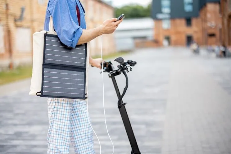 man on electric scooter with small foldable solar panel hanging out of tote bag on his soldier