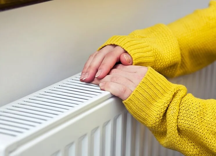woman in yellow jumper warming her hands on radiator