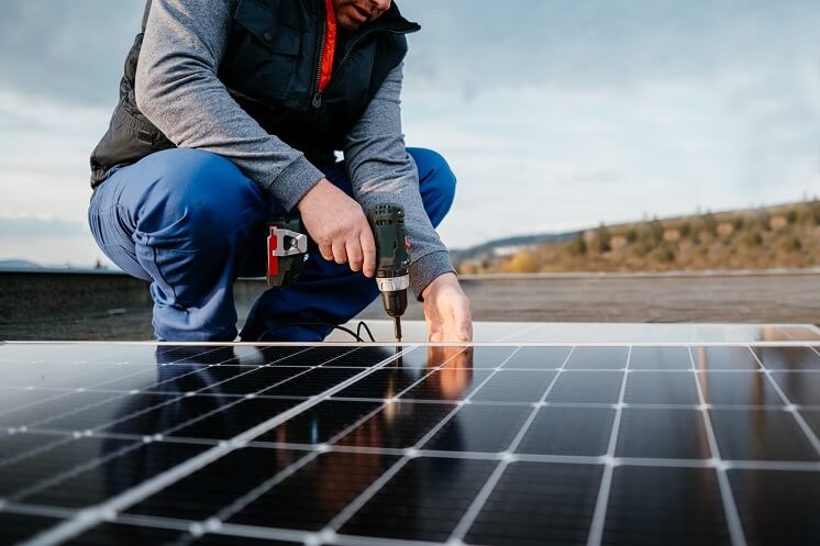 Someone using a drill to secure DIY solar panels onto the roof