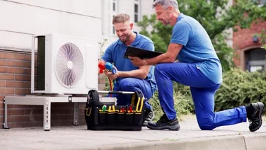 two men in blue uniforms next to an external heat pump unit on a house