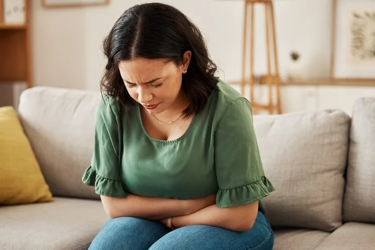woman sitting on sofa clutching her stomach in pain