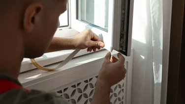 A view behind of someone putting excluder strips on an open double glazed window