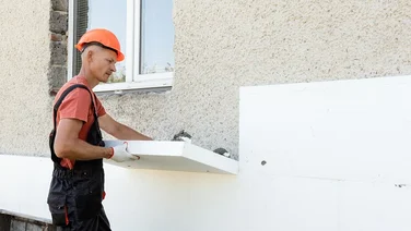 Contractor installing external wall insulation on outside of house