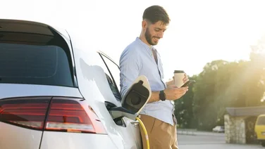 Man looking at phone smiling while electric car charges at a public charging point