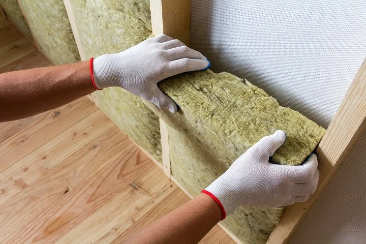 Person wearing white gloves slotting insulation blocks of fibreglass into a wall