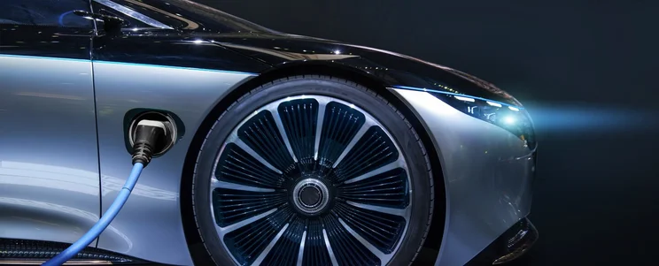the side view of an electric car with its headlights on, shining to the right