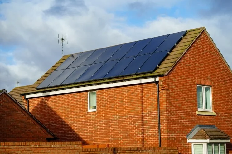 a redbrick house with solar panels against a cloudy sky