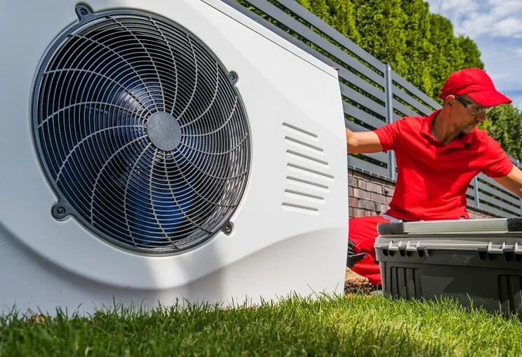 outdoor unit of a heat pump being worked on by a technician in red uniform