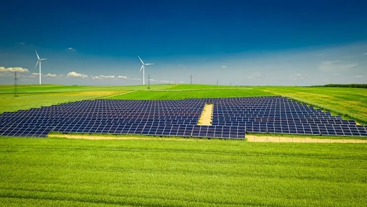 solar panels and wind turbines in a field, under a blue sky