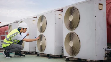 an engineer in a fluorescent jacket checking on heat pumps on a roof